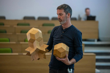 The artist Dominic Hopkinson, holding several wooden polyhedra.