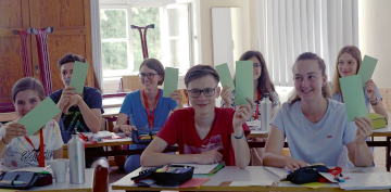 Several students holding up green cards, smiling at the camera.